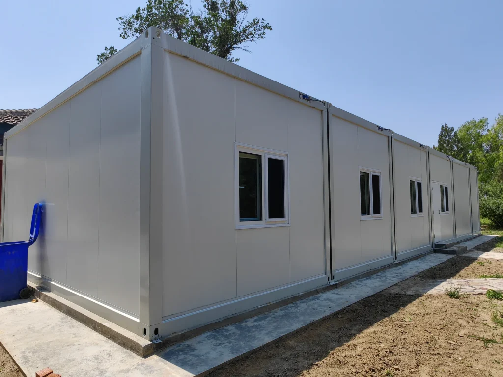 Single-storey white modular building with windows and an entrance beside a concrete walkway