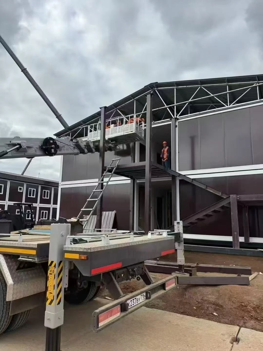 Crane and workers installing two-storey modular camp buildings at a project site