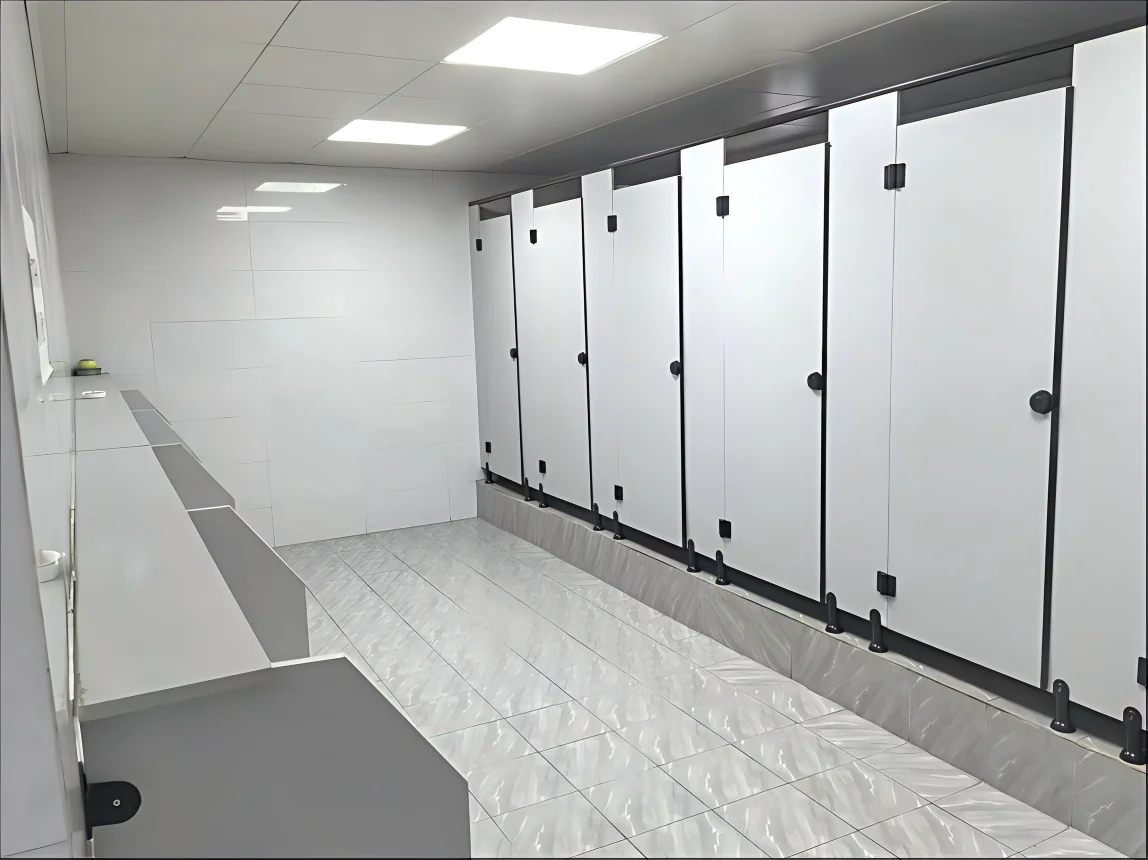 Washroom interior with a row of white toilet cubicles and a long counter opposite