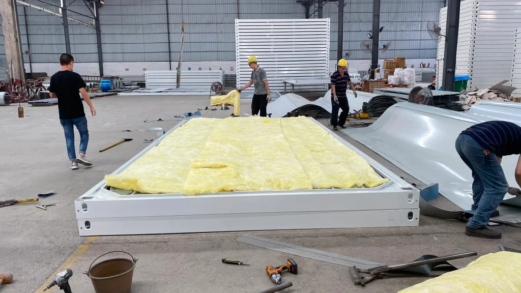 Factory workers placing fibrous insulation in a framed KUBO roof assembly before the outer sheet is fitted